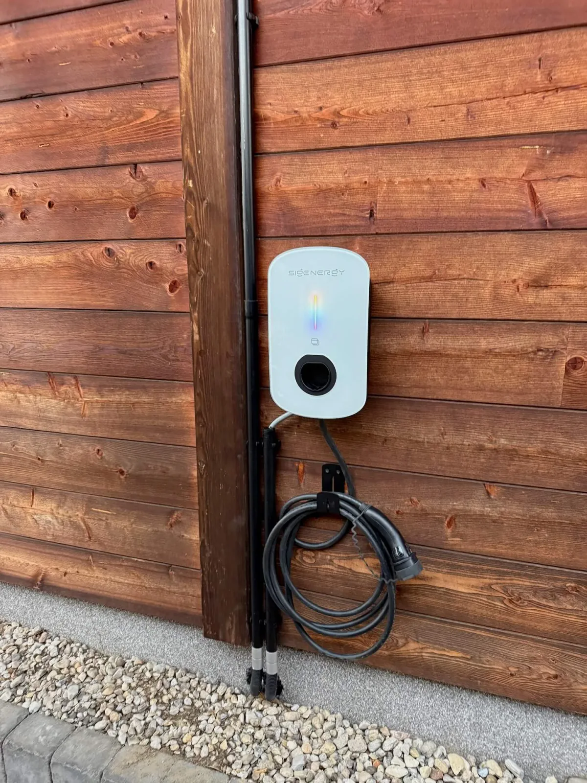 Sigenergy AC Charger Wallbox montiert an einer Holzfassade mit Ladekabel