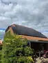Dach eines Hauses mit Ziegeln, Solarmodulen und grünem Bewuchs an der Hauswand.