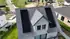 Dach eines Hauses mit drei Gruppen schwarzer Solarmodule und einem Dachfenster, umgeben von weiteren Häusern und Straßen.