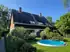 Haus mit braunem Dach, Solarmodulen, Garten und rundem Aufstellpool unter blauem Himmel.